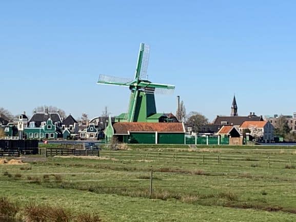 Groene windmolen in Zaanse Schans met op de achtergrond traditionele Nederlandse huizen en een heldere hemel.